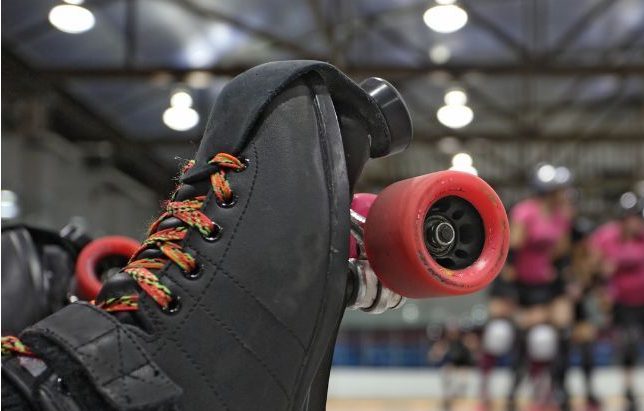 close up photo of roller skate resting one its heel with blurred roller derby players in background