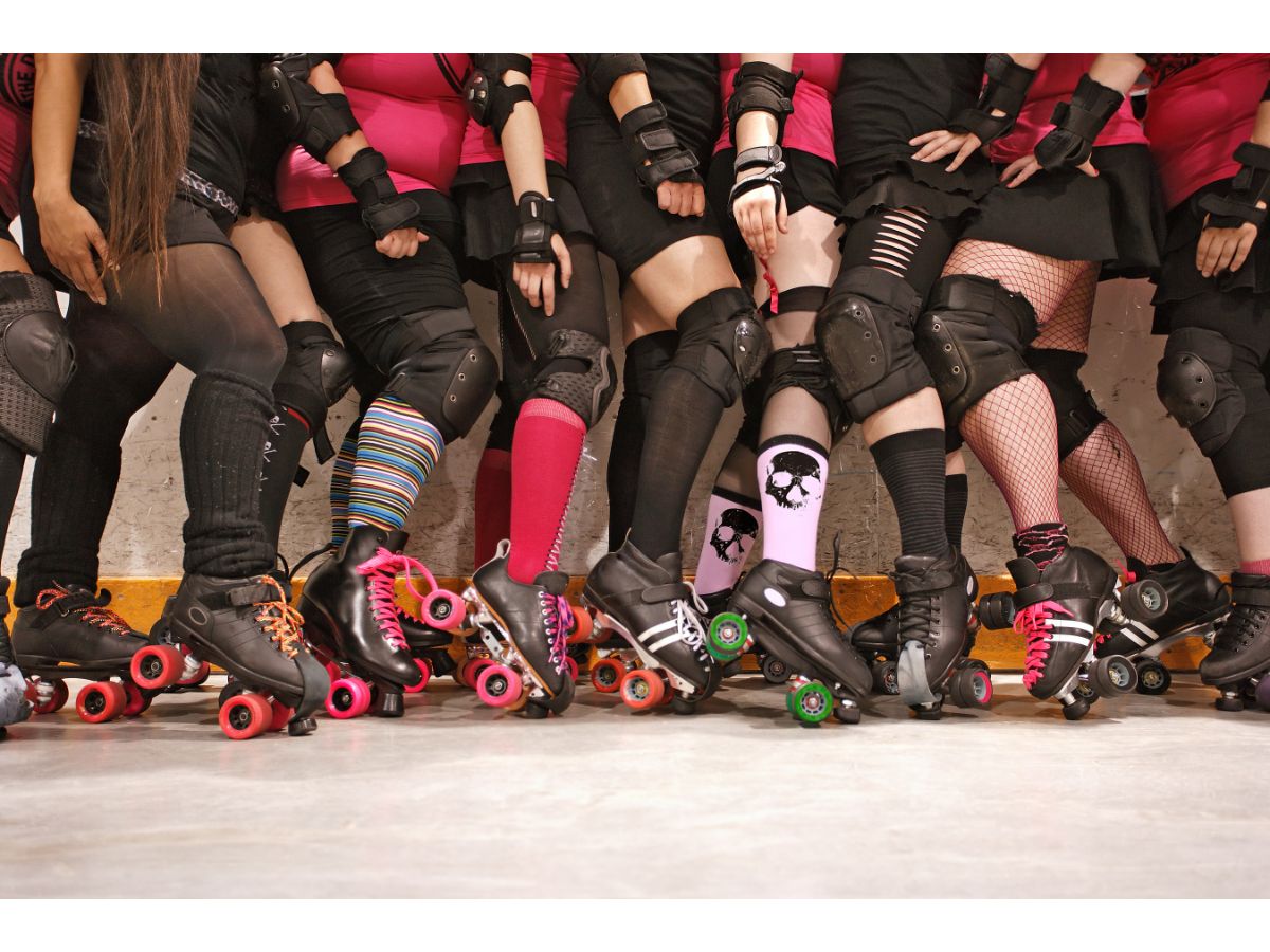 photo showing group of roller derby skaters legs, kneepads, socks and skates with with mostly pink and black colors